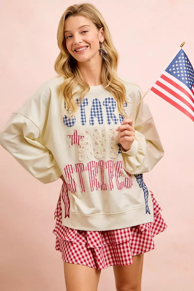 Woman wearing 4th of July sweatshirt with patches, holding American flag, showing patriotic style.