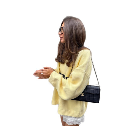 Woman wearing a yellow Letter-print Loose-fit Sweater, holding a black clutch, posing stylishly outdoors.
