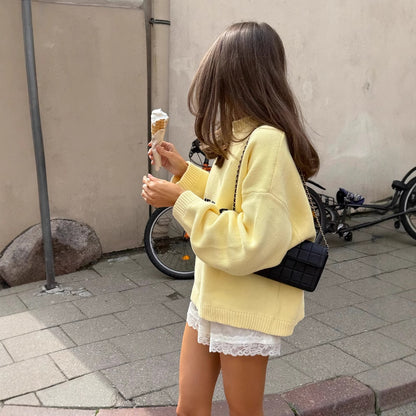 Woman wearing a yellow Letter-print Loose-fit Sweater, holding a black clutch, posing stylishly outdoors.
