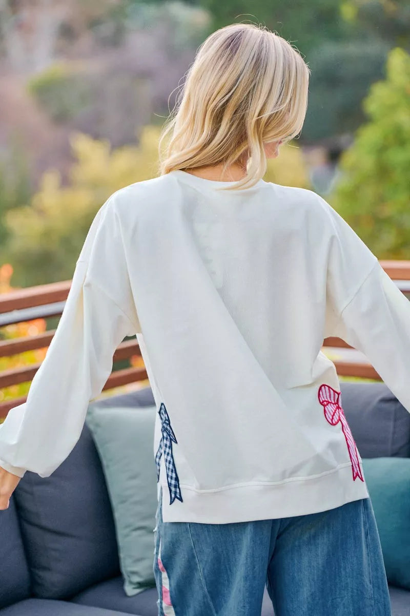 Back view of a woman wearing a cream 4th of July sweatshirt with blue gingham and pink striped patches.