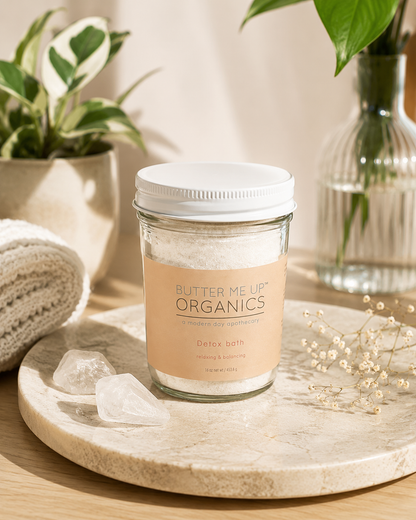 Detox bath soak with essential oils in a glass jar on a natural wooden surface with greenery and decorative stones.