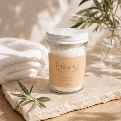 Detox bath soak with essential oils in glass jar by Butter Me Up Organics on a stone surface.