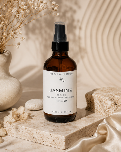 Jasmine Essential Body Oil in an amber bottle on a textured surface with floral accents.