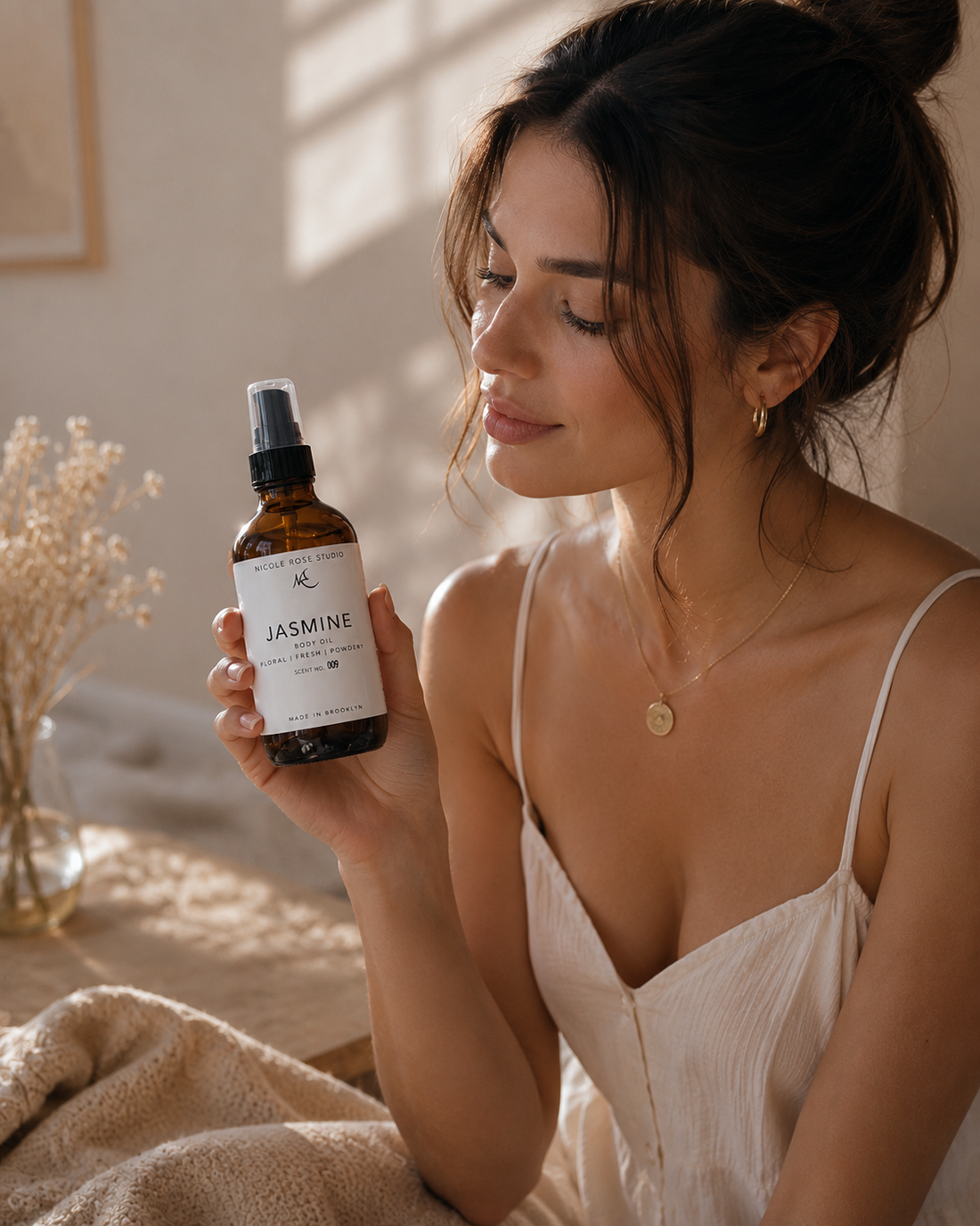 Model holding jasmine essential body oil in a sunlit room with soft, calming decor.