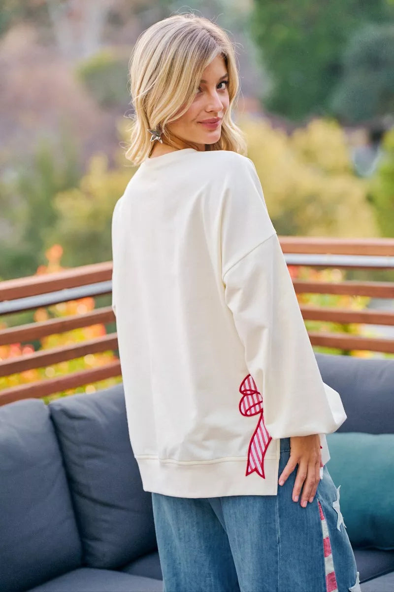 Back view of a woman wearing a cream-colored 4th of July sweatshirt with patches, stylishly posing outdoors.