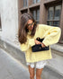 Woman wearing a yellow Letter-print Loose-fit Sweater, holding a black clutch, posing stylishly outdoors.